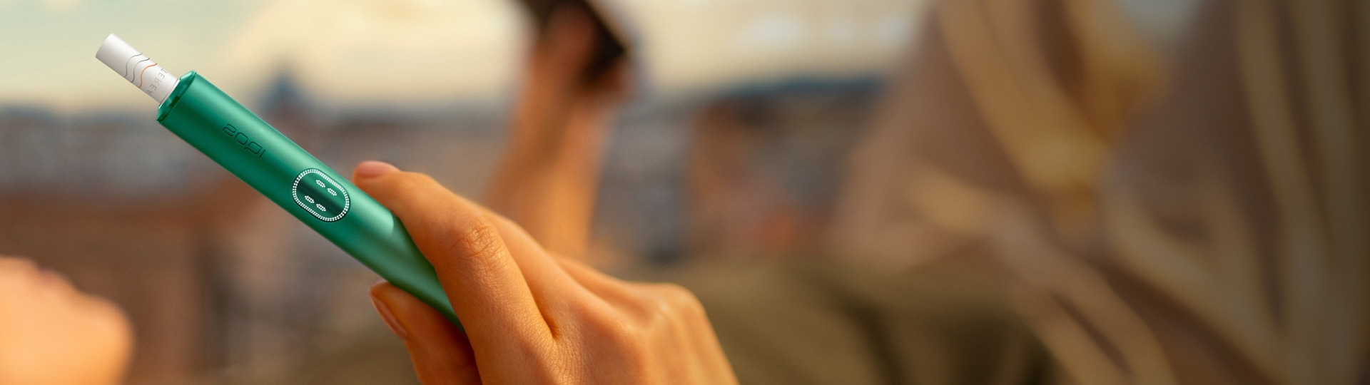 امرأة تحمل جهاز IQOS وهي تنظر إلى جهاز كمبيوتر محمول.